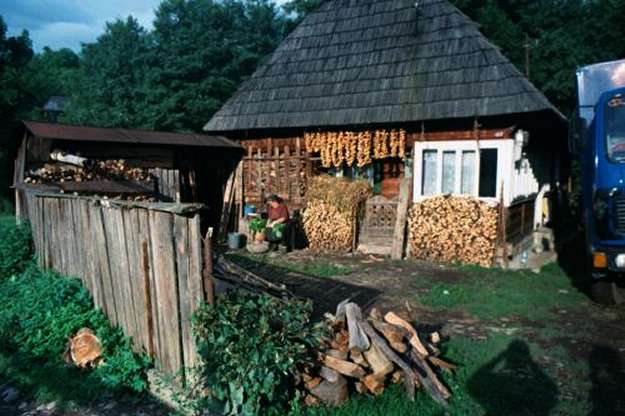Typical farm house with steep roof, woodpiles, drying peppers, cook cleaning vegetables.